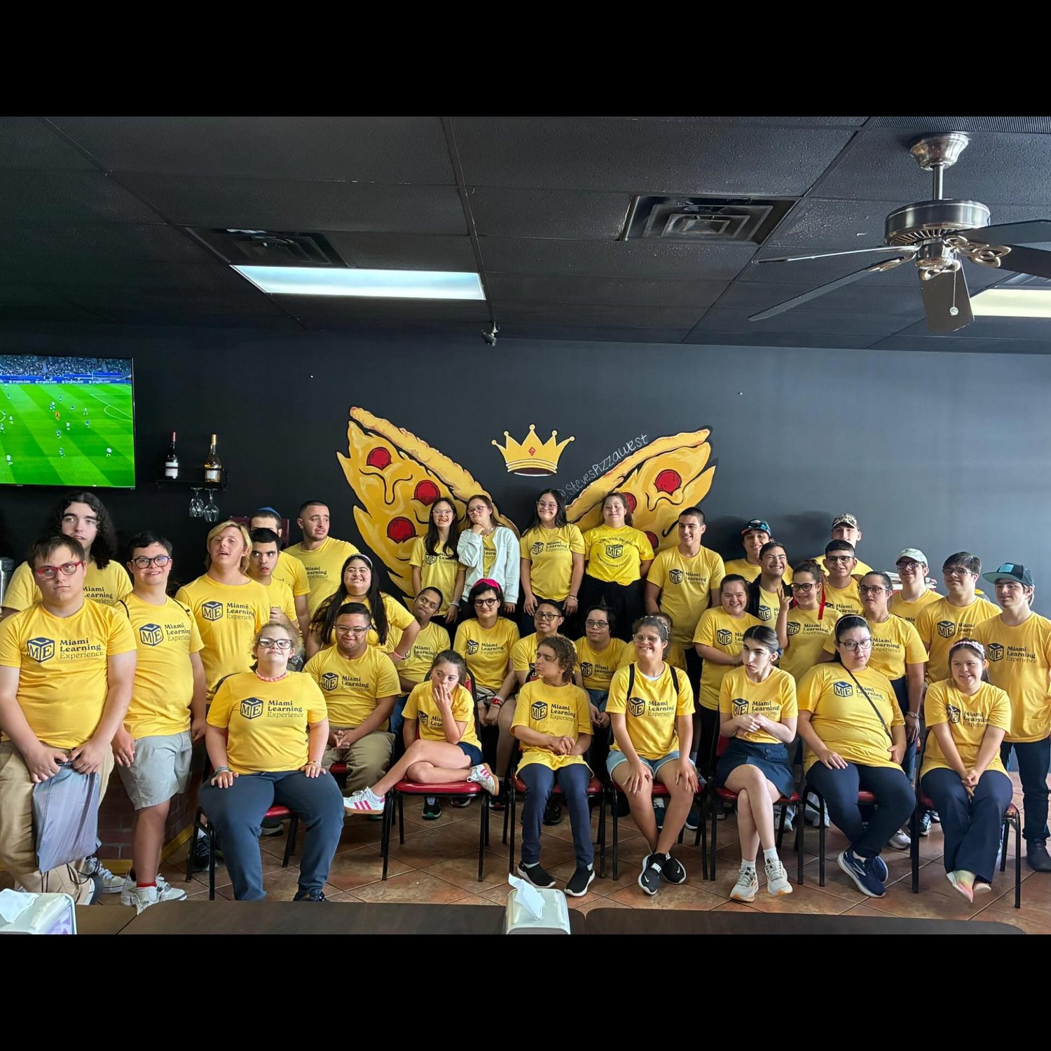 Large group posing in front of the pizza, wings, and crown mural