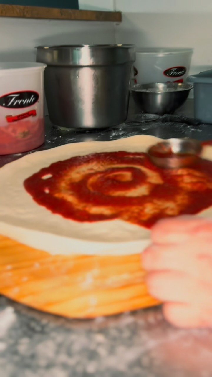 Homemade sauce being swirled onto fresh raw dough